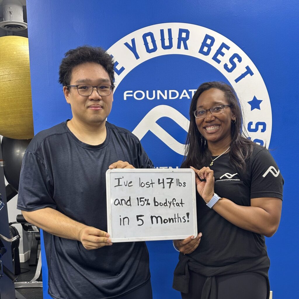 A Foundation Fitness client holding a sign with the weight and body fat they lost, standing with their trainer